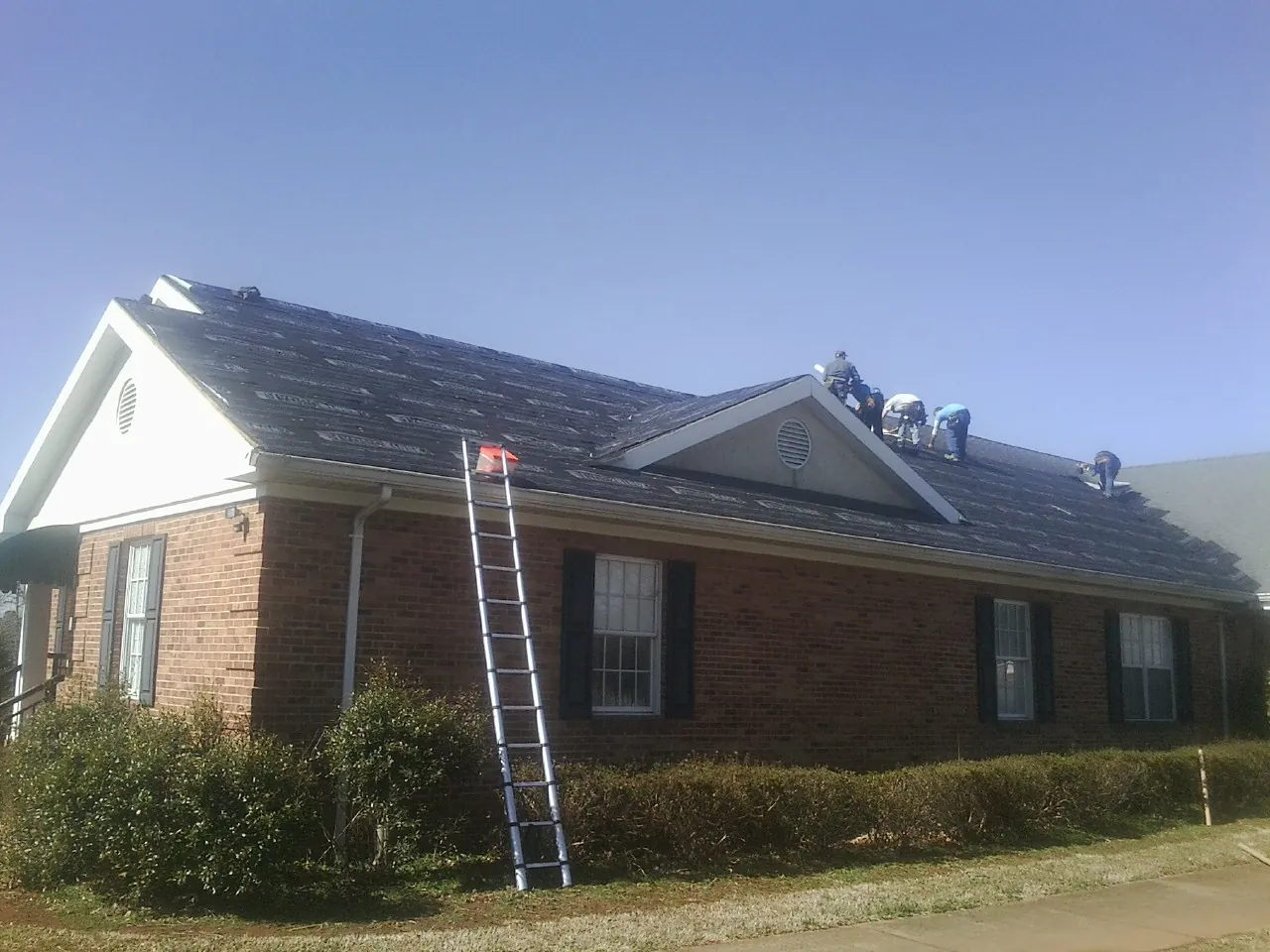 Crew tearing shingles off a brick ranch roof with a ladder set — Metal Roof Repair work by our crew in Anna