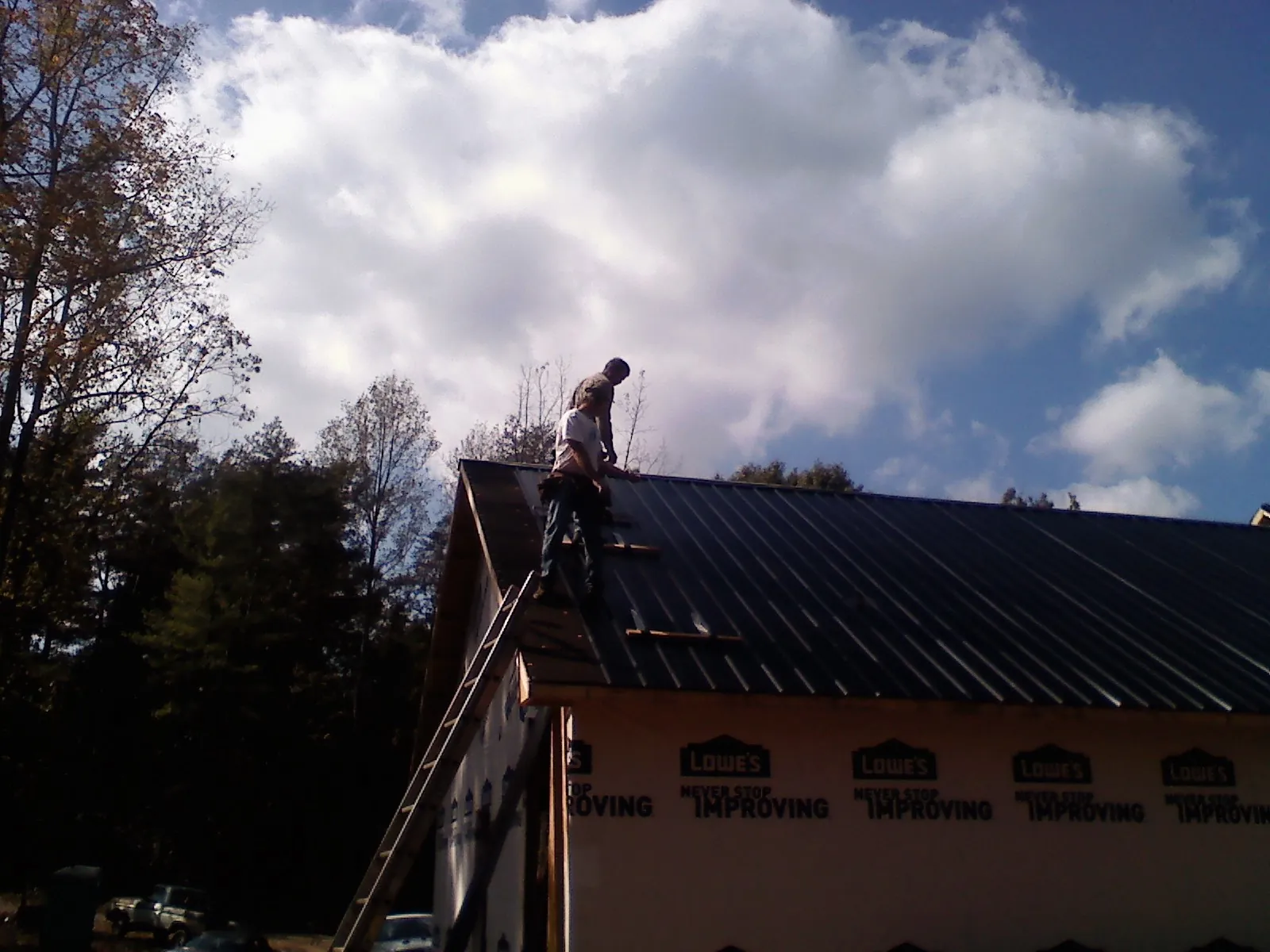 Roofer fastening dark metal panels high against a cloudy sky, from a Roof Inspection job in Anna